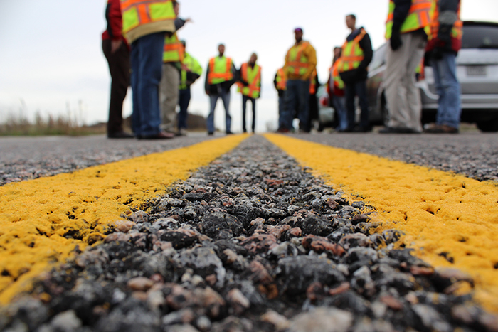 Cose up view of a highway centerline with multiple people wearing safety vests in the background