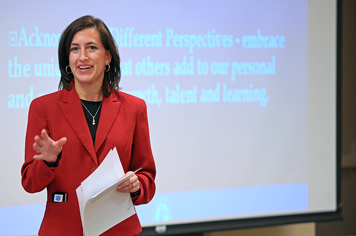 Woman in a Red suit stands in front of projection screen