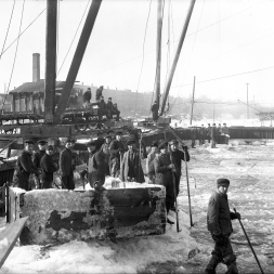 Clearing ice out of Cofferdam #7. The work was continued over the winter, and the engineers took precautions to keep the concrete from freezing. This included not pouring concrete when the air temperature was below zero, covering the forms with tarps, and heating them. The sand and rock bins for the concrete were also heated and the large buckets carrying concrete were dipped in hot water